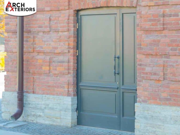 Exterior view of a brick building with a dark double door and a downspout running along the wall