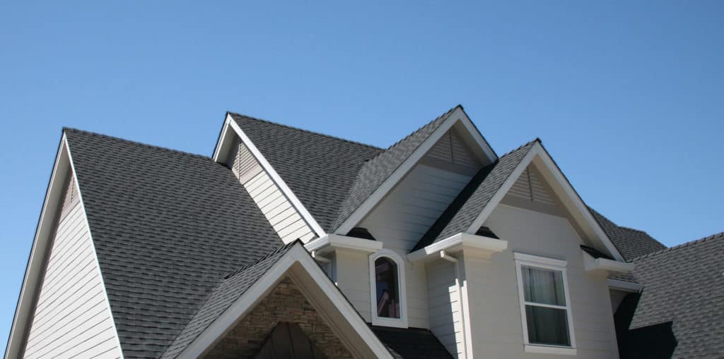 house with multiple gabled roofs, gray shingles, and light-colored siding against a clear blue sky