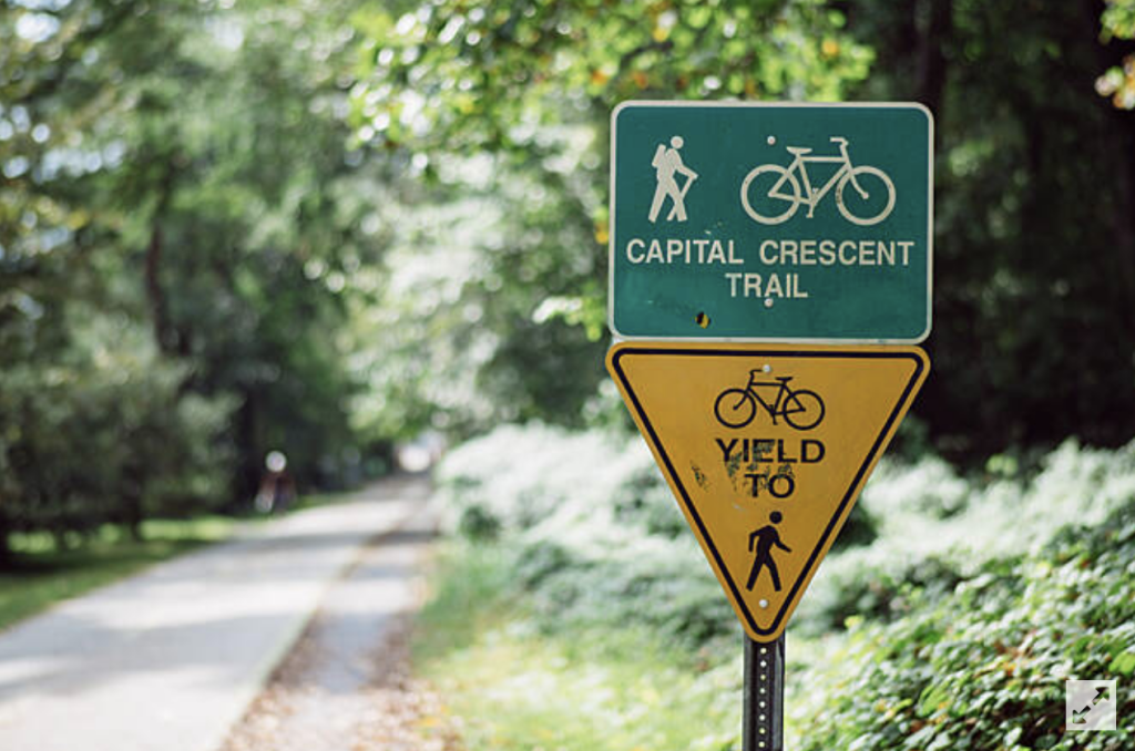 capital crescent trail head sign in front of blurred background of the trail - things to do in bethesda