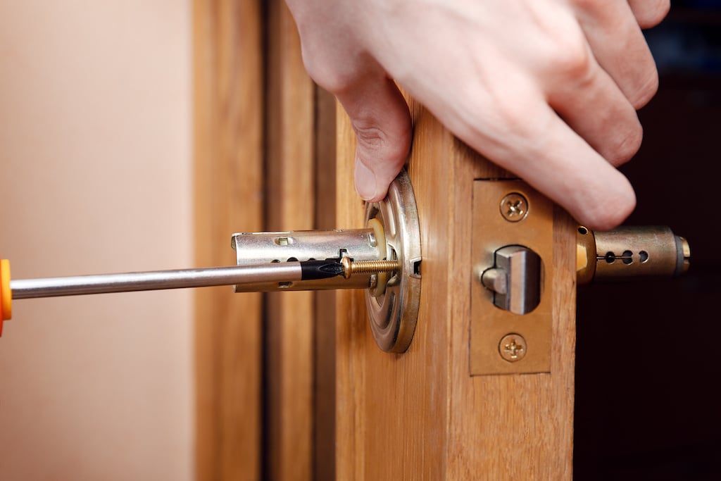 pair of hands tightening screws on doorknob during exterior door installation