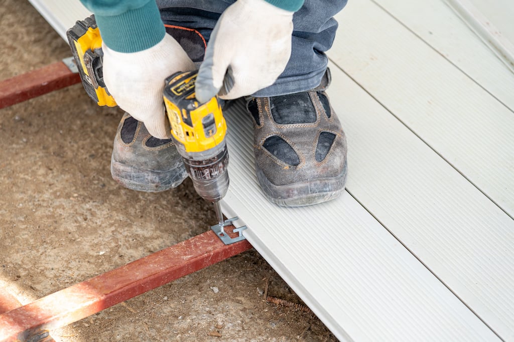 man installing composite decking to joint with drill and fasteners