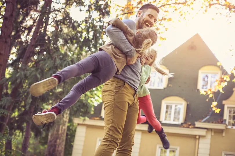 A father plays with his children outside their home, emphasizing the need for reliable roofing service