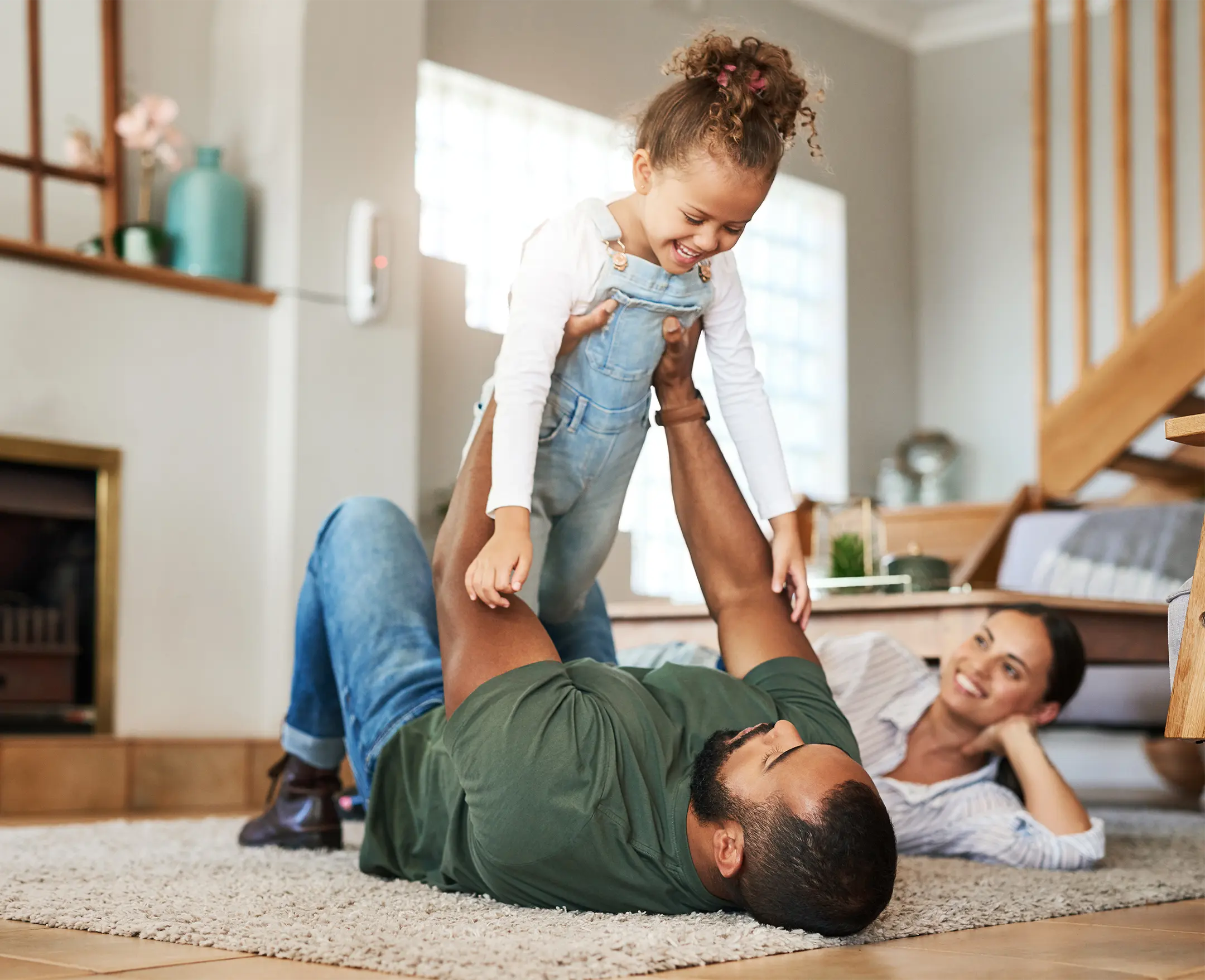 father on floor holding daughter above him with wife smiling in the background