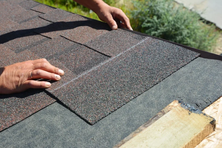 close up of a pair of hands installing asphalt shingles on roof
