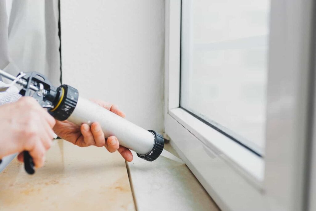 pair of hands installing caulk on a window pane replacement job
