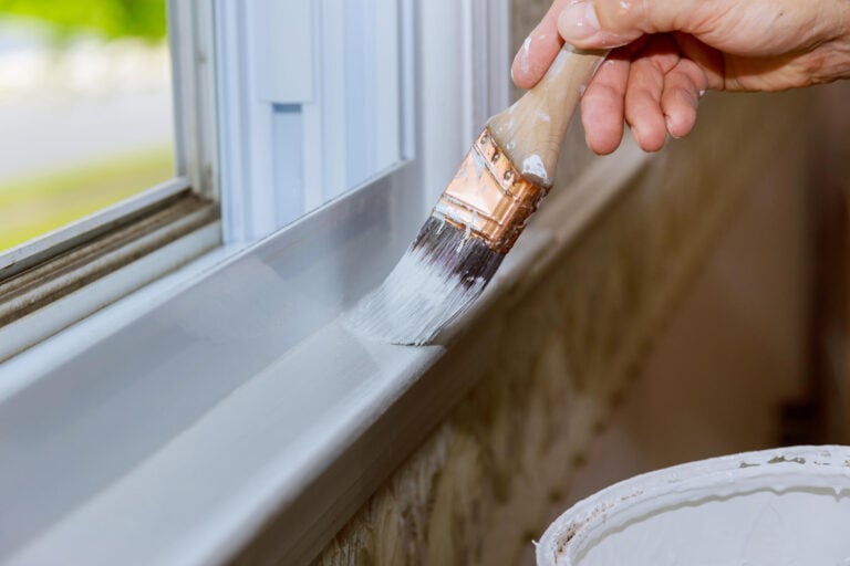 window painting ideas-cloe up of a person adding a fresh coat of white paint to interior window trim