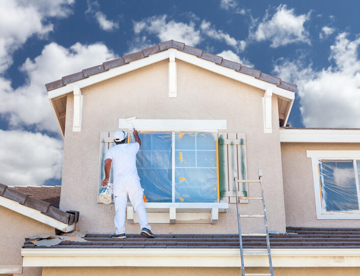 window painting ideas-male painter standing on a roof painting the trim around exterior windows