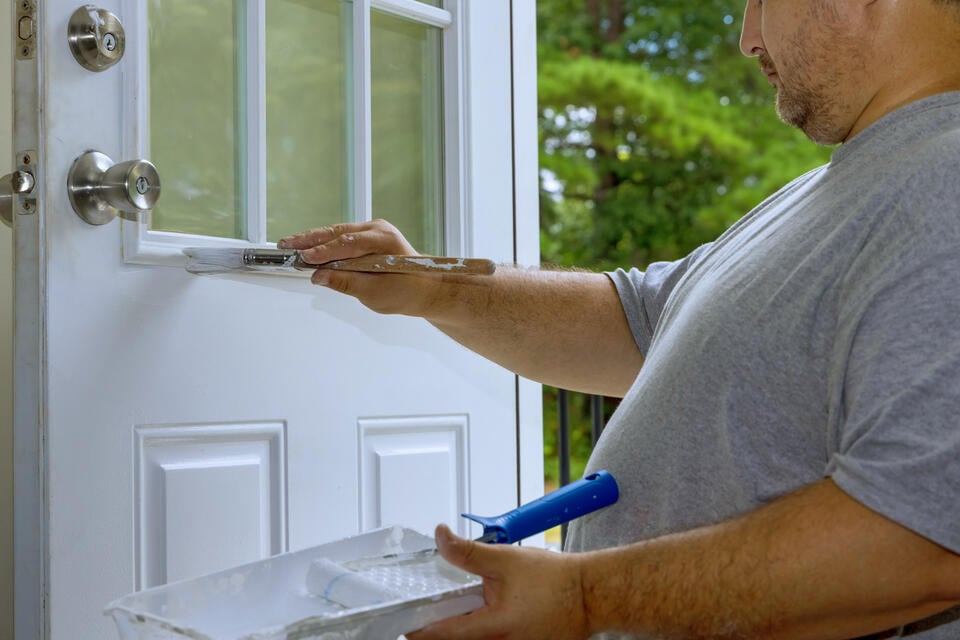 how to paint a fiberglass door-man holding a paint tray and hand painting a front door white