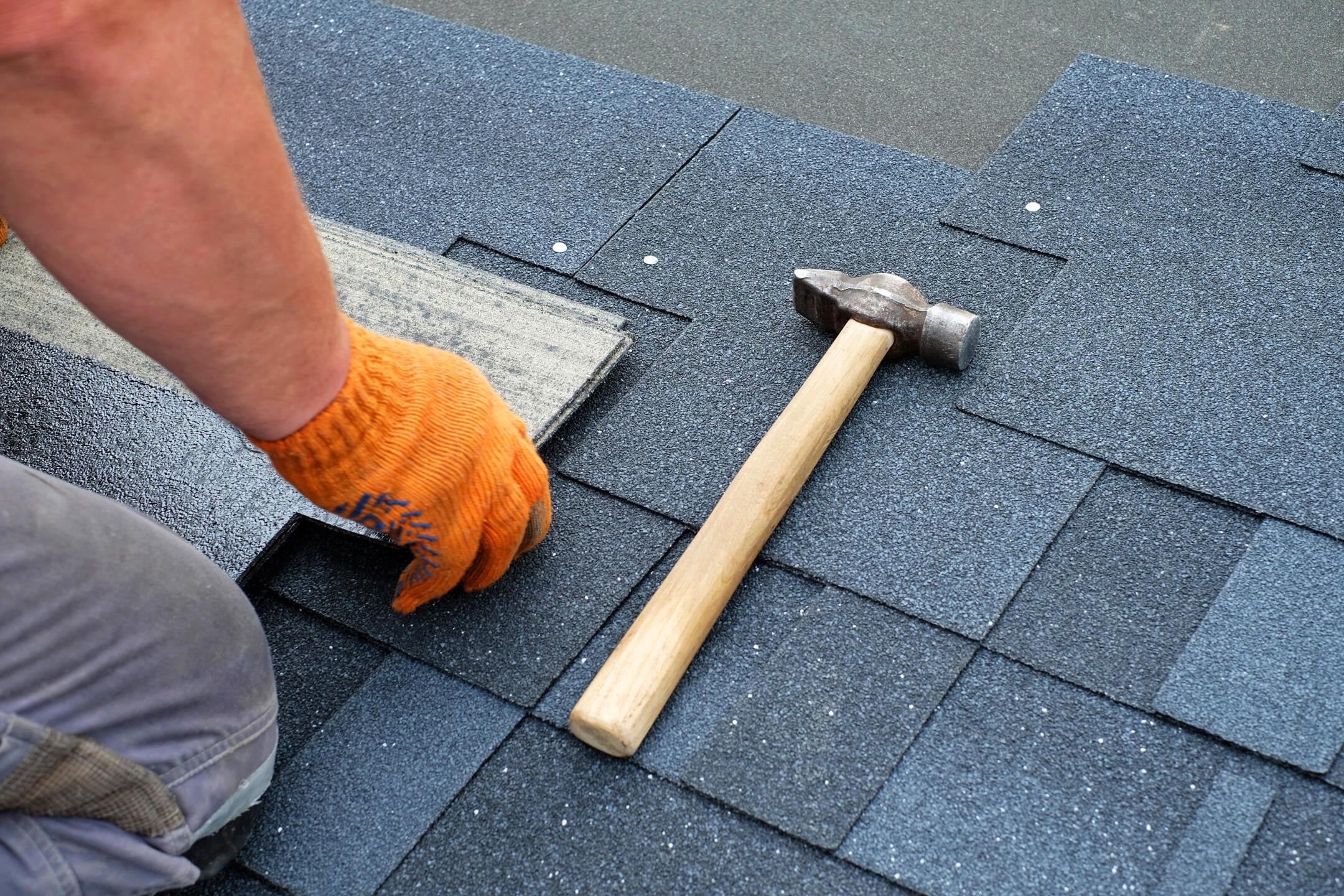 dimensional shingles-close up of man wearing gloves and using nail and hammer to install architectural shingles