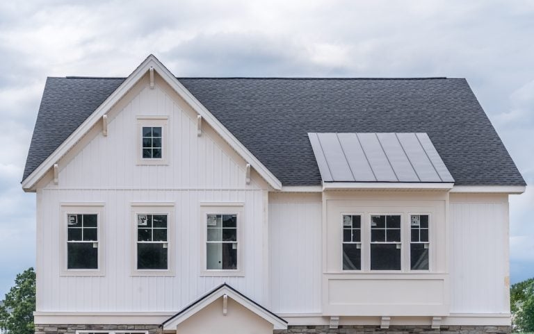 White vertical lap siding facade of newly built single family home with gable and bay window on a new American neighborhood street