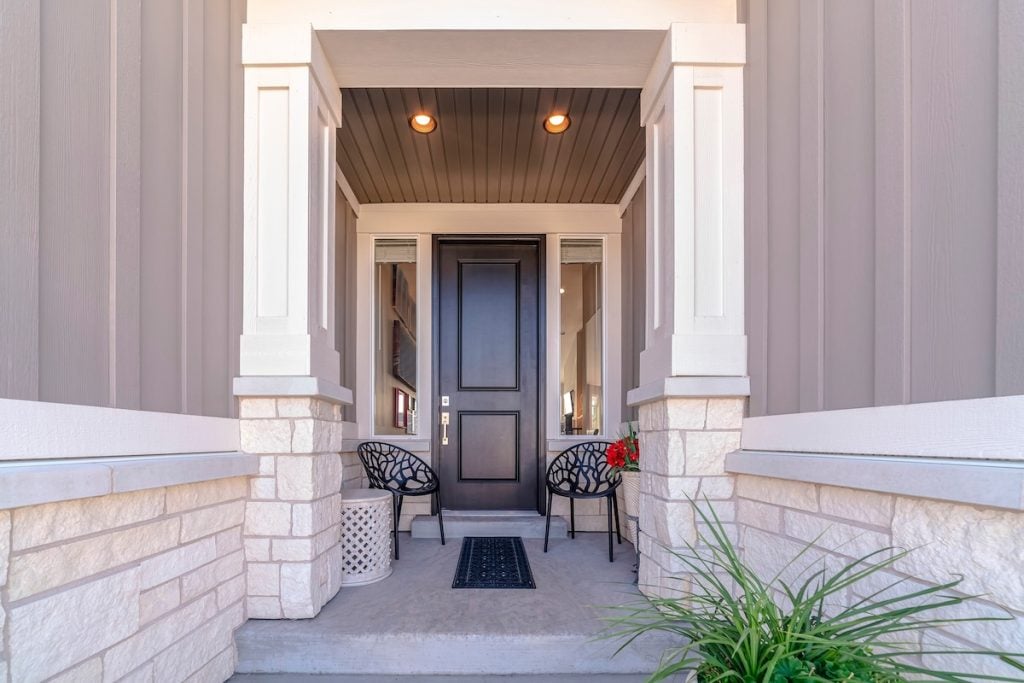 Path leading to front door of a residential house. Path leading to a front door of a residential house with covered porch with two chairs and mat and timber clad walls
