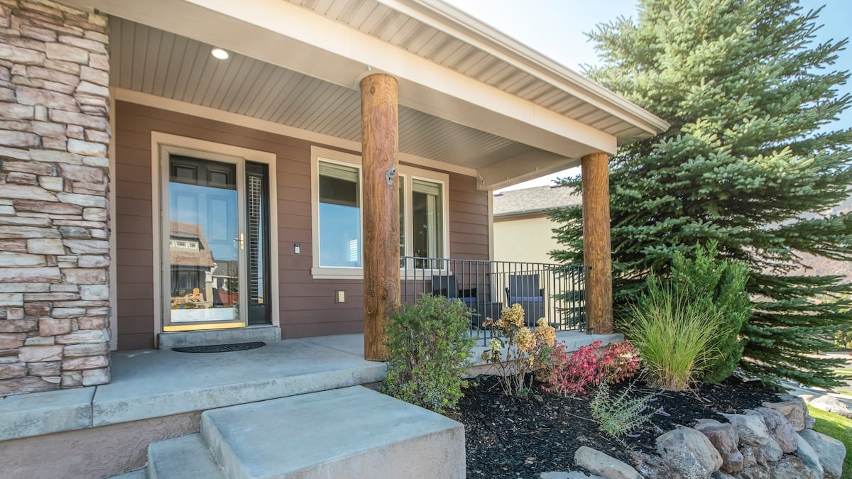 Pano Front exterior of a house with a raised edge landscape and stone brick walls. A porch with storm door, windows and log posts with a steel railings, and a concrete stairs near the garage with bricks. steel door