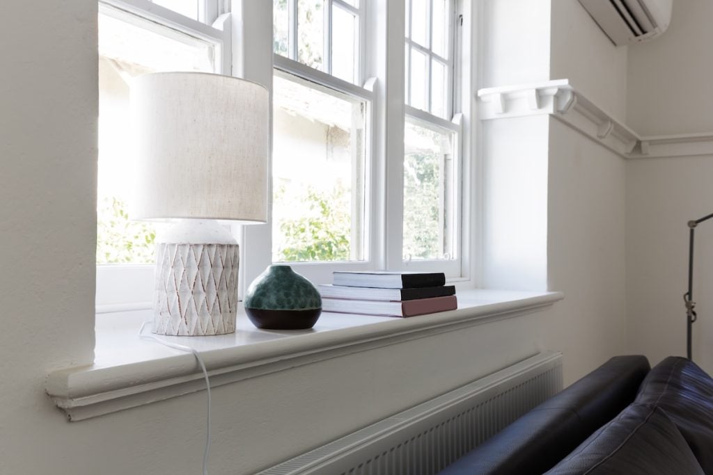 A classic white sash window, complete with multiple glass panes, is prominently centered against a dark, textured brick wall. The rich, deep hues of the brickwork are  what is a window sash contrasted by the lighter mortar joints, creating a distinctive pattern. A solid stone lintel sits above the window, complemented by a simple sill below. The bright white frame stands out, reflecting subtle elements from the surrounding environment. This architectural detail captures the essence of a residential or urban structure, ideal for depicting housing, construction, renovation projects, or general building designs in editorial or commercial contexts.