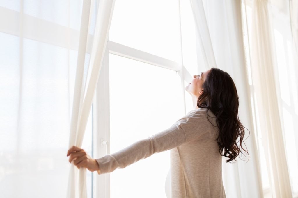 pregnancy, motherhood, people and expectation concept - close up of happy pregnant woman opening window curtains