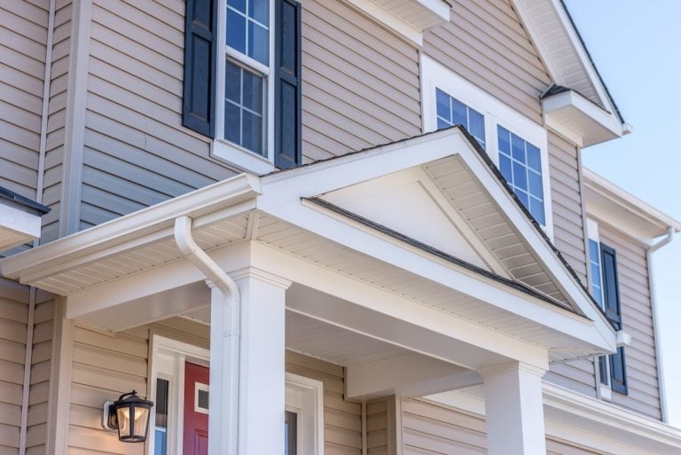 Portico leading to the entrance of vinyl horizontal lap siding covered building, with a roof structure over a walkway, supported by white rectangular columns on a new single family home