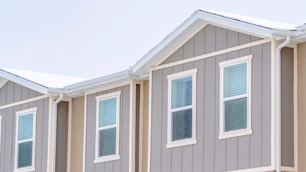vertical siding vs horizontal siding Panorama Snowy roof brick wall and vertical siding at exterior of townhome against sky. Residential landscape with view of the upper storey of townhouses.