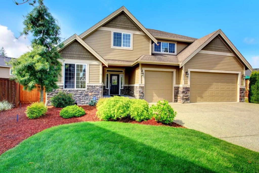insulated vinyl siding Clapboard siding house  with stone trim. View of  entrance porch, beautiful flower bed with green lawn, bushes and fir tree