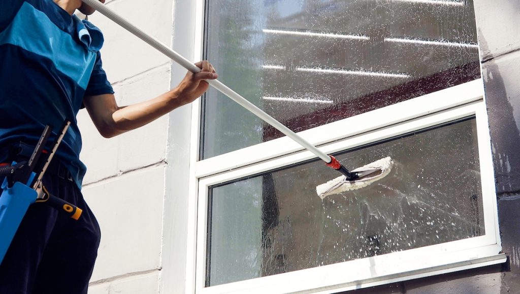 professional window cleaning Male professional cleaning service worker in overalls cleans the windows and shop windows of a store with special equipment.