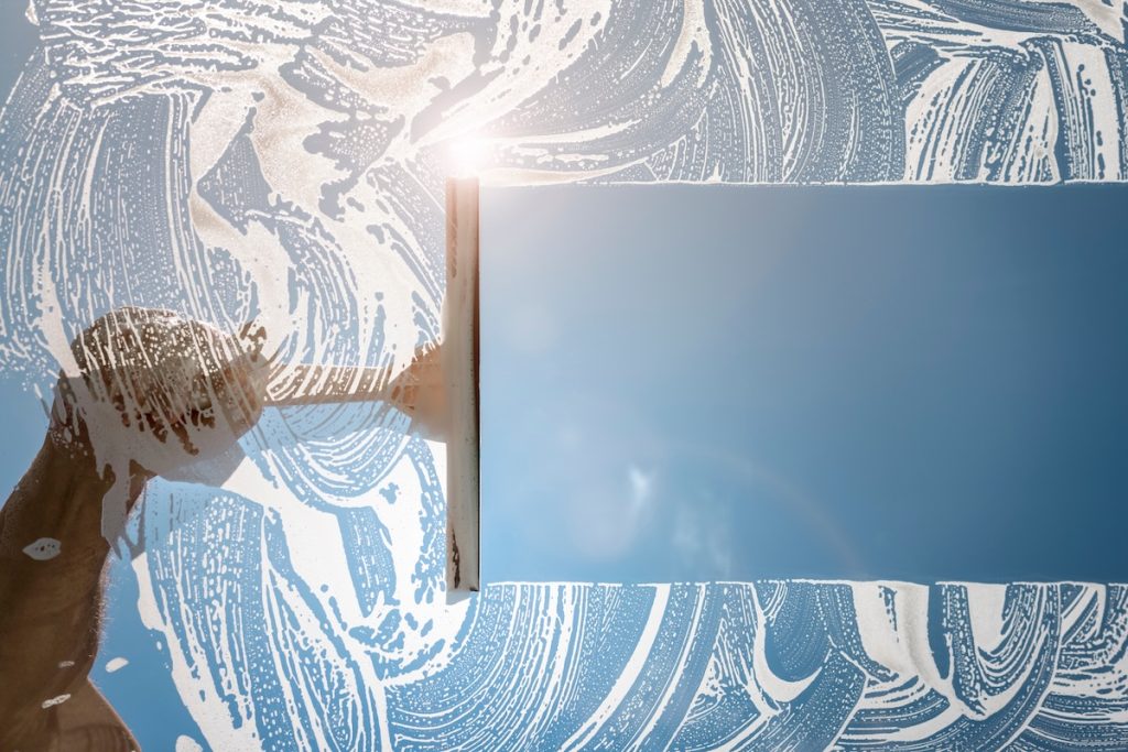 professional window cleaning Window cleaner using a squeegee to wash a window with clear blue sky