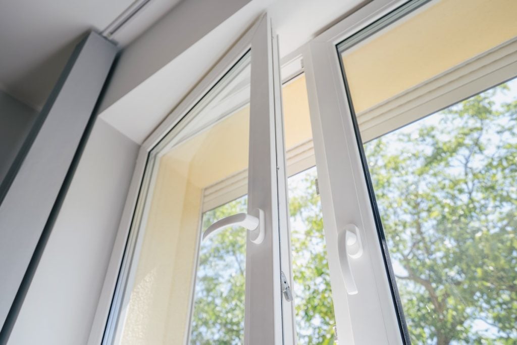 window warranty low angle view of plastic pvc window with white metal frame installed at modern house, blurred green trees outside the room