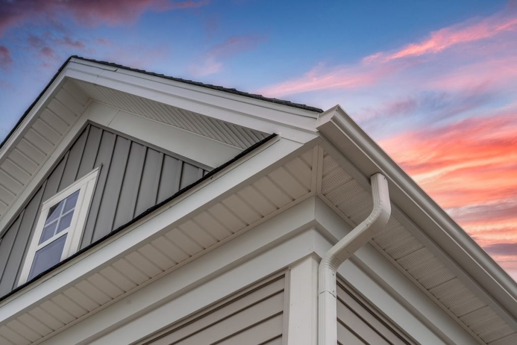 vertical siding vs horizontal siding White frame gutter guard system, with gray horizontal and vertical vinyl siding fascia, drip edge, soffit, on a pitched roof attic at a luxury American single family home dramatic sunset sky