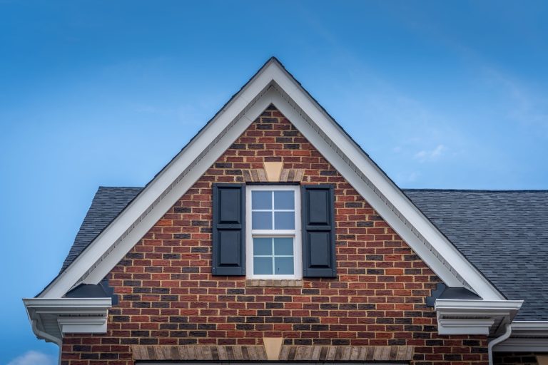 Gable with red brick facade siding, double hung window with white frame, vinyl shutters on a pitched roof attic at a luxury American single family home neighborhood