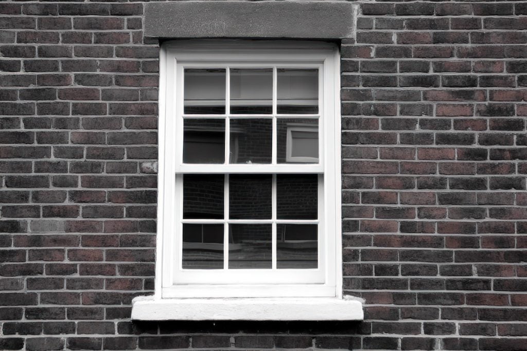 where to buy window sash replacement kit A classic white sash window, complete with multiple glass panes, is prominently centered against a dark, textured brick wall. The rich, deep hues of the brickwork are contrasted by the lighter mortar joints, creating a distinctive pattern. A solid stone lintel sits above the window, complemented by a simple sill below. The bright white frame stands out, reflecting subtle elements from the surrounding environment. This architectural detail captures the essence of a residential or urban structure, ideal for depicting housing, construction, renovation projects, or general building designs in editorial or commercial contexts.