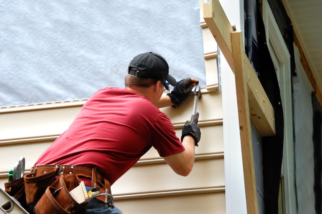 siding maintenance Young homeowner installs siding to his home.  He is holding a hammer and wearing a tool belt.