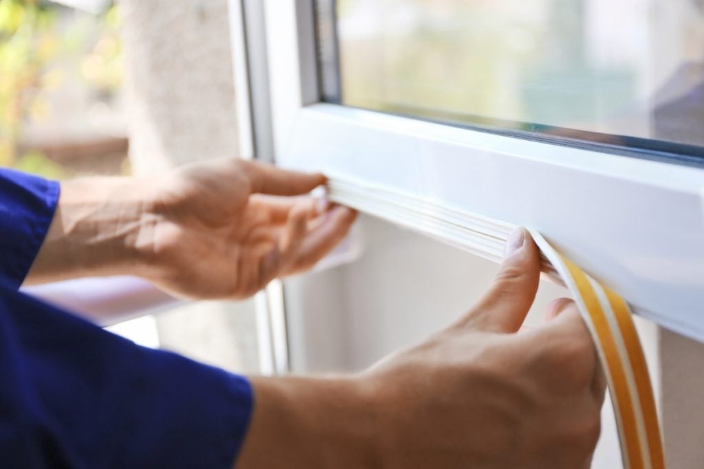 Construction worker putting sealing foam tape on window in house window seal repair