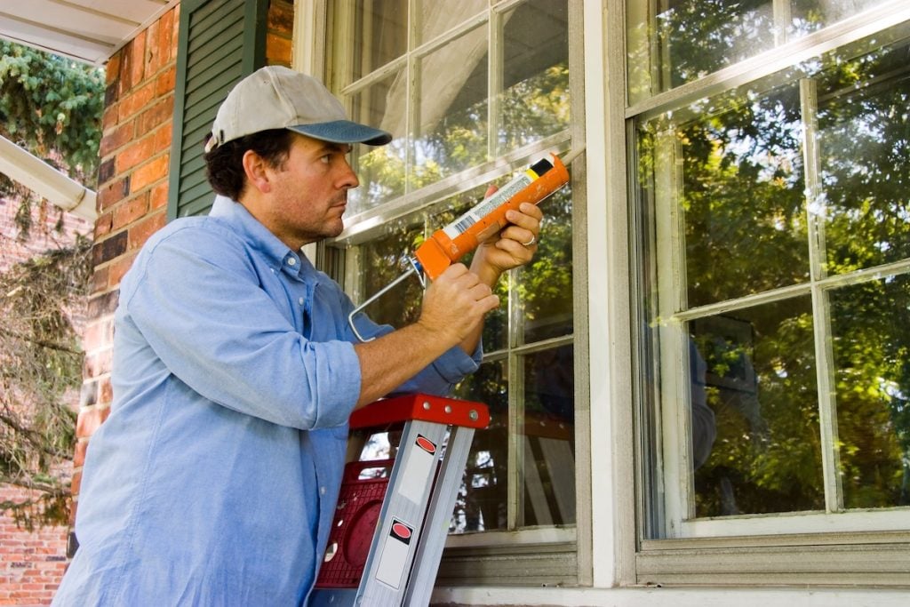 Man on ladder caulking outside window window seal repair