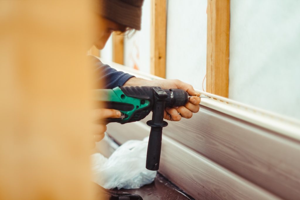siding installation cost A worker installs panels beige siding on the facade of the house