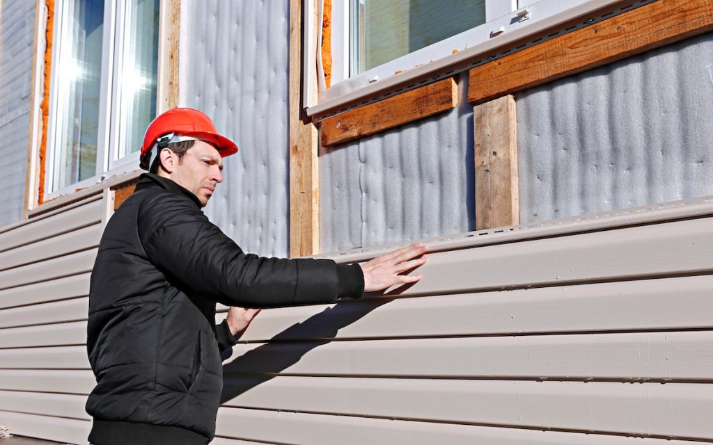 siding installation cost A worker installs panels beige siding on the facade of the house