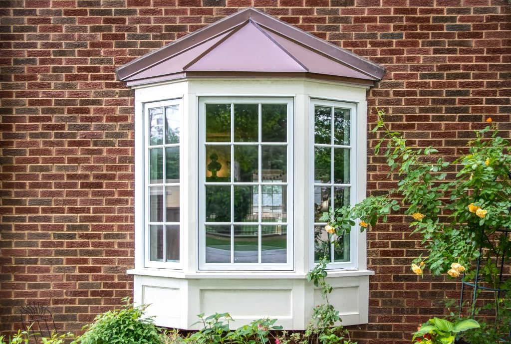 bay window Bay window with copper roof on traditional brick home with flowers below and yellow roses extending out onto the window in springtime