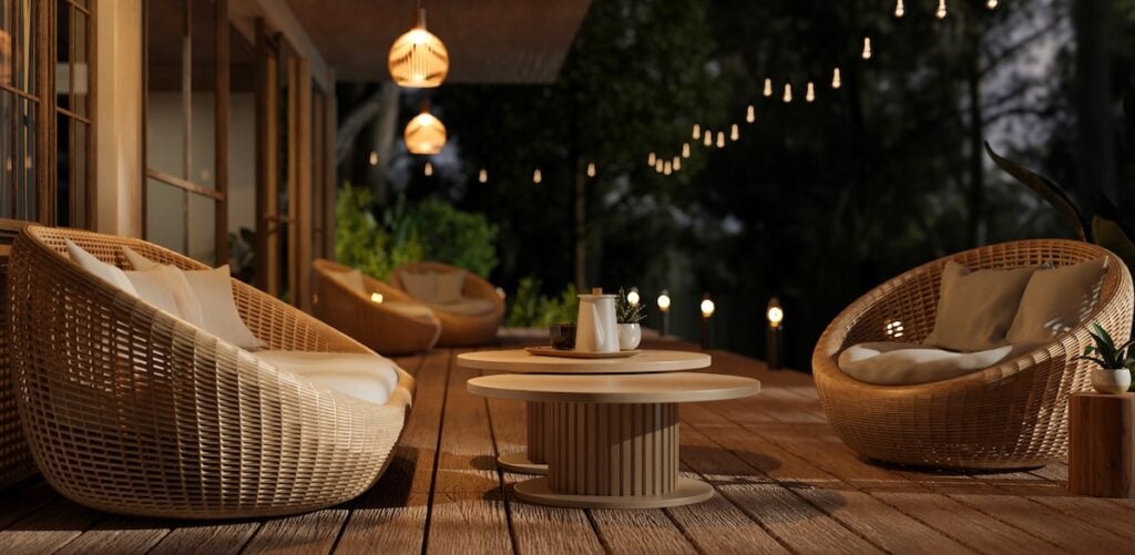 deck lighting ideas Side view of a beautiful deck with cosy round wicker armchairs, outdoor string lights and a beautiful nature view at night. Hotel or restaurant outdoor lounge. 3d render, 3d illustration