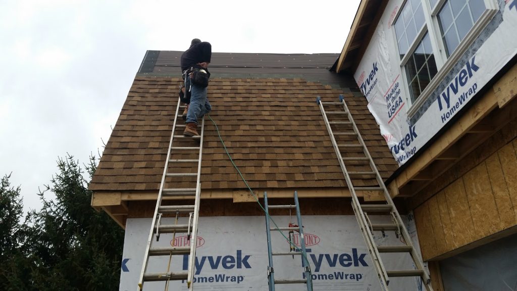 factors influencing roof lifespan brown shingles roof worker on top of roof using ladder